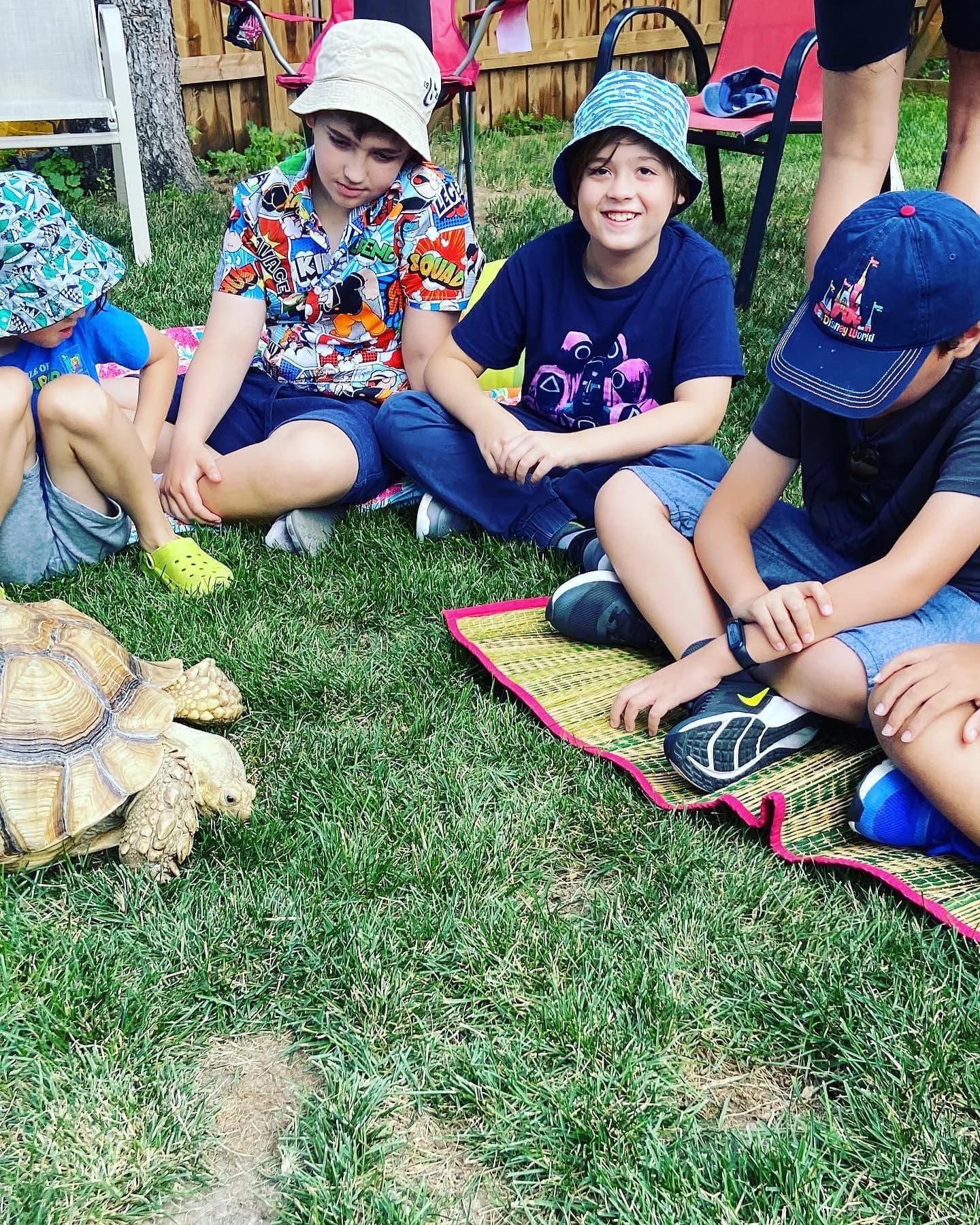 Group of young guests sitting around a sulcata tortoise on a blanket at a Hands On Exotics birthday party