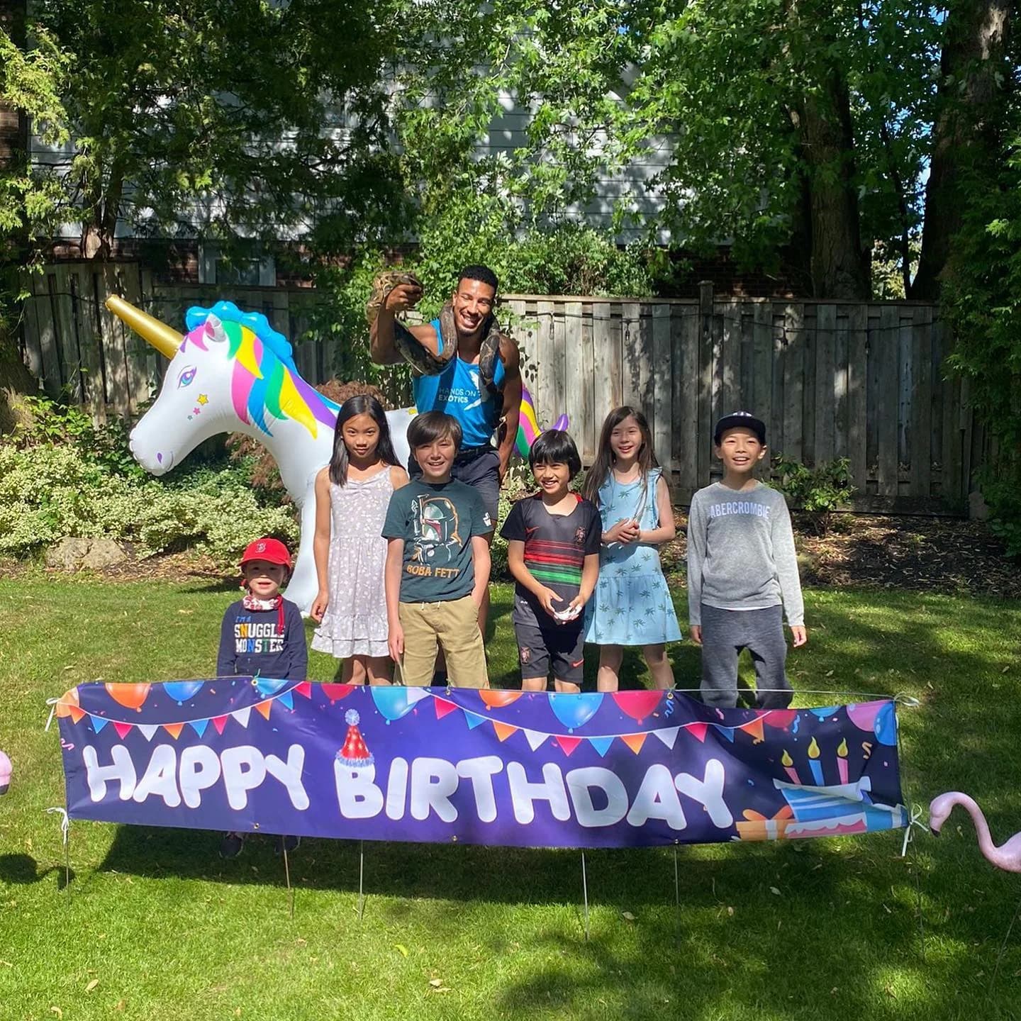 Children gathered with a handler beside a Happy Birthday banner at a Hands On Exotics backyard birthday party