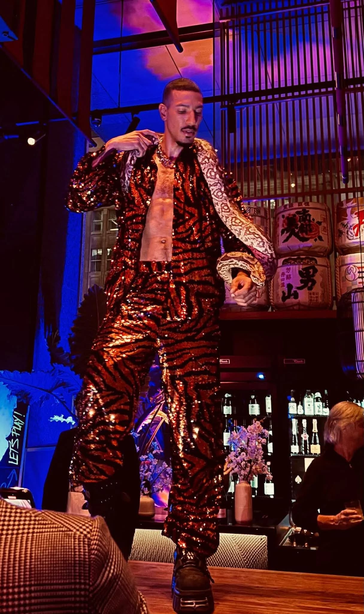 A performer in a glittering tiger-print outfit stands on top of the bar at Chotto Matte during a high-energy nightclub event