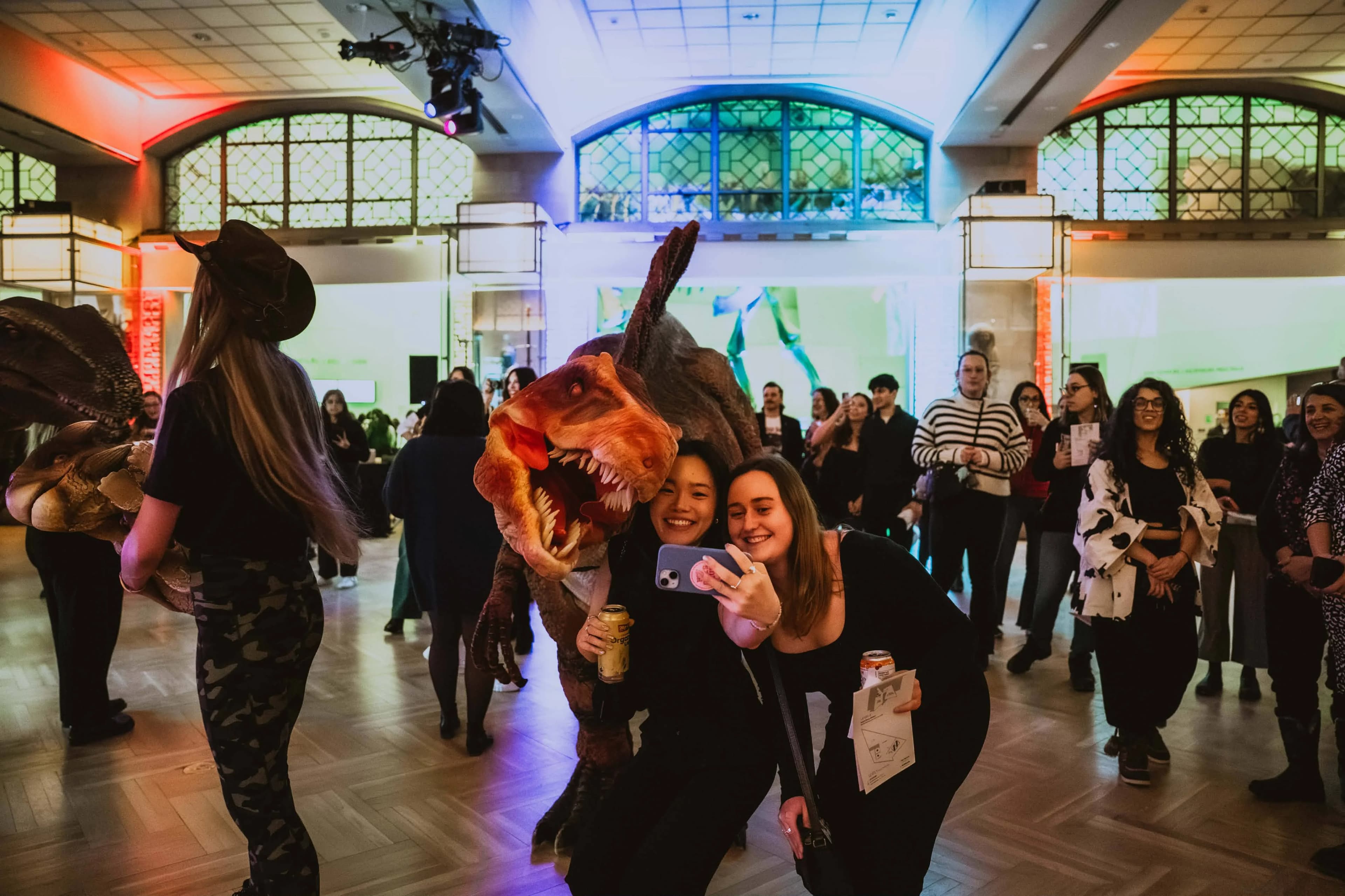 Guests at a ROM After Dark gala laugh and take a selfie with a life-sized animatronic dinosaur inside the museum rotunda